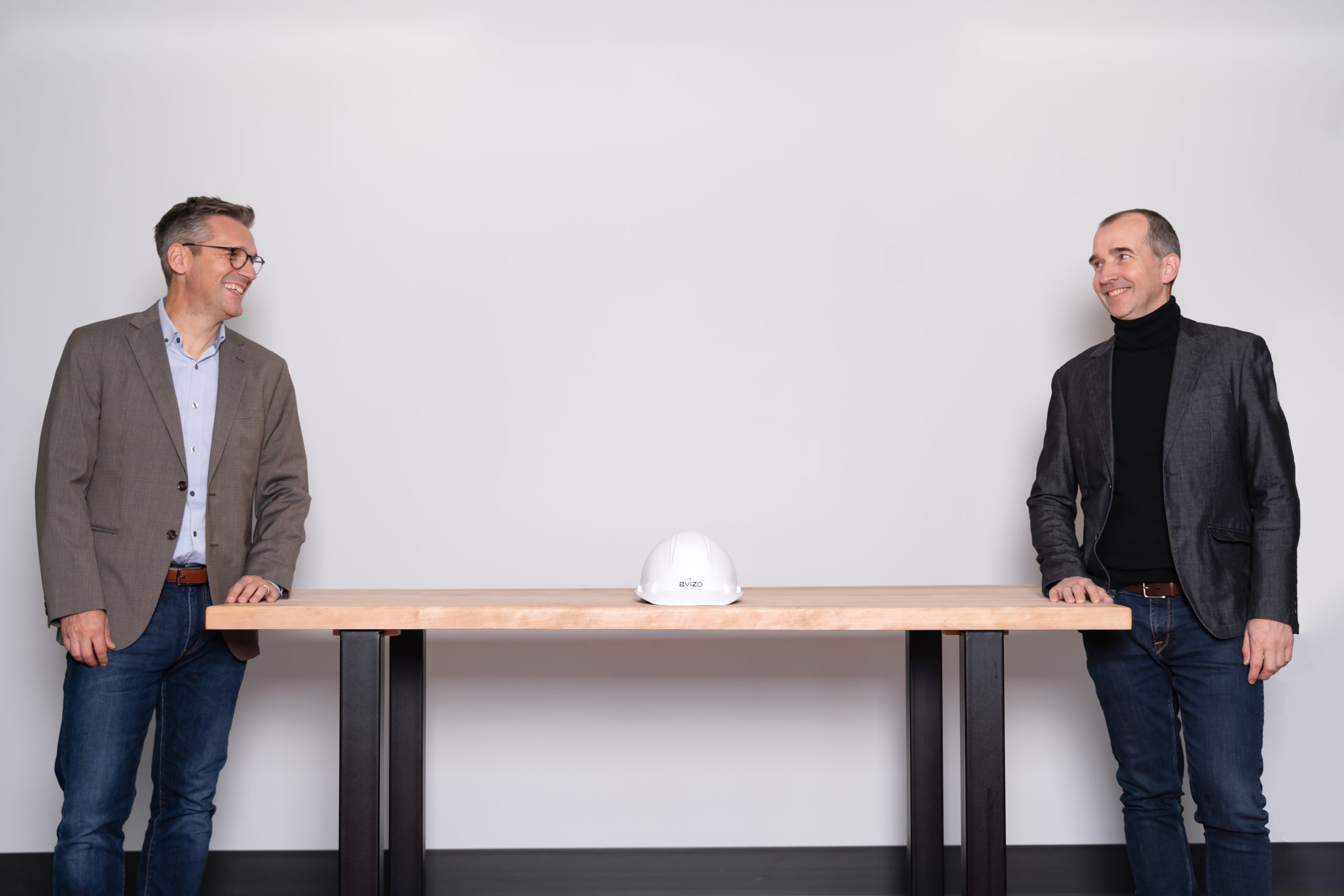 Deux hommes en vestion se tiennent debout à chaque bout d'une sur laquelle se trouve un casque de construction blanc