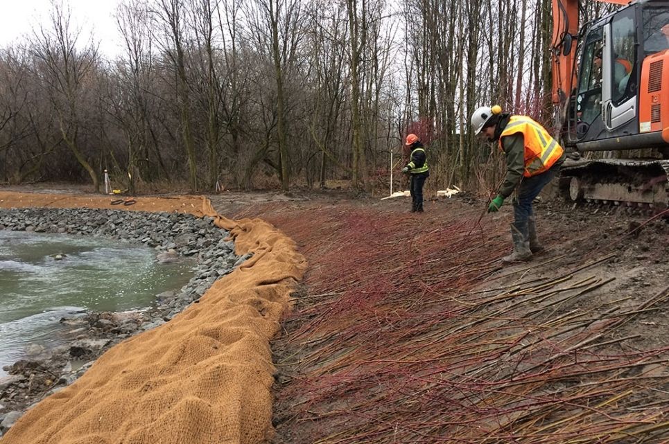 Deux employés s'affairent sur les rives d'une rivière