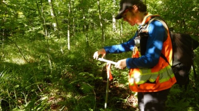 Un homme en forêt utilise un outil pour échantillonner le sol