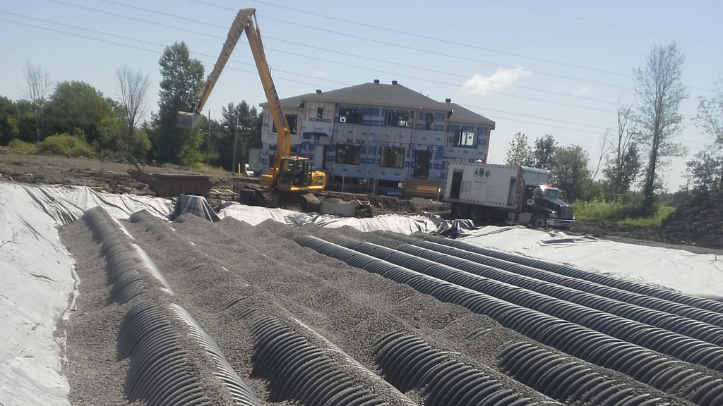 Des chambres d'infiltration en cours de remblaiement avec une maison en construction.