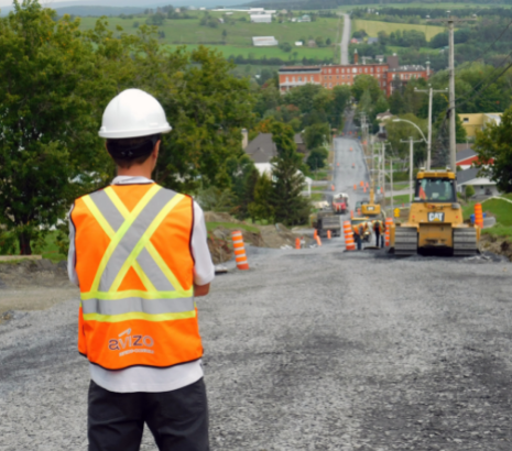 Un homme portant un casque de sécurité et une veste haute visibilité se tient devant un chantier routier