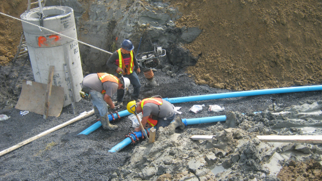 Trois employés de chantier travaillent au fond d'une fosse à connecter des conduites d'aqueduc
