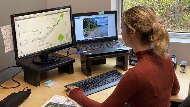 Une femme travaille à son ordinateur sur ses écrans un plan et une photo d'une berge